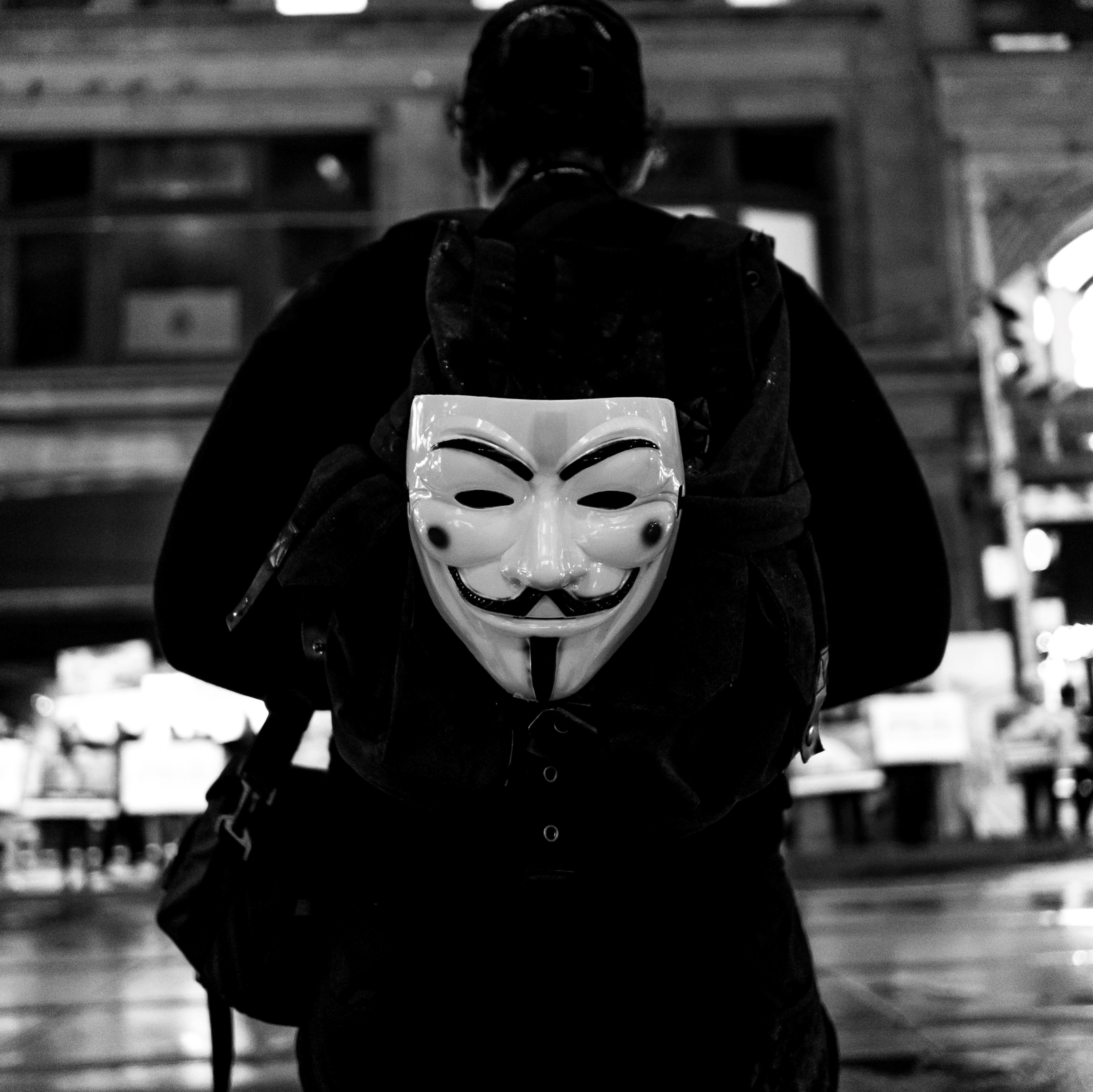 Photographie d'un individu portant dans son dos le masque symbole des Anonymous