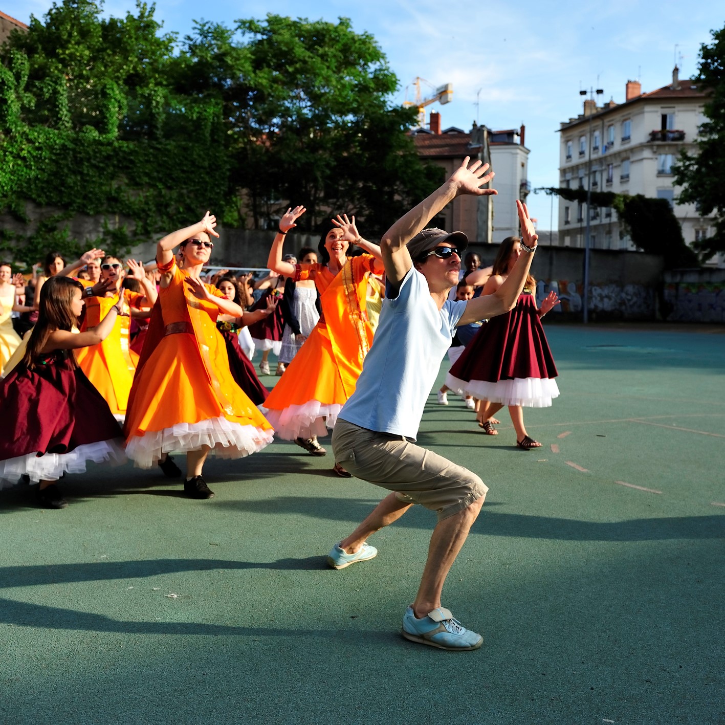 Photo de danseurs en costumes traditionnels (robes et châles) en train de répéter avec leur chorégraphe sur un terrain de basketball