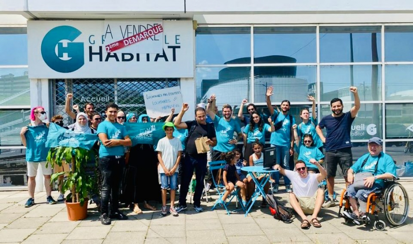 Photo des membres d'Alliance Citoyenne devant le bâtiment de Grenoble Habitat, tenant une pancarte "Locataires pas écoutés, locataires méprisés", habillés en T-shirts avec le logo d'Alliance Citoyenne
