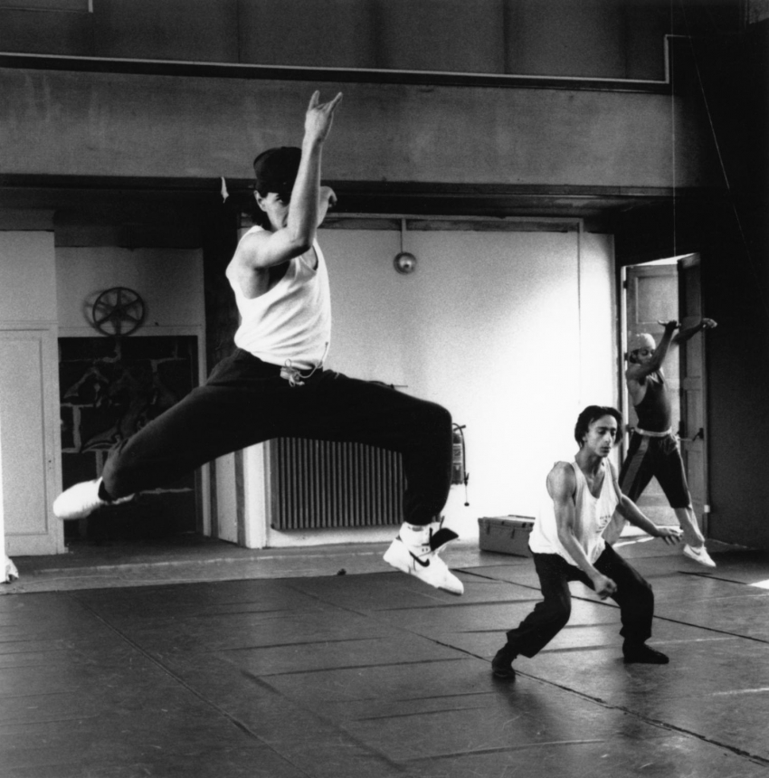 Photo d'une répétition de danse de hip-hop, un jeune homme en train de sauter avec le bras devant son visage